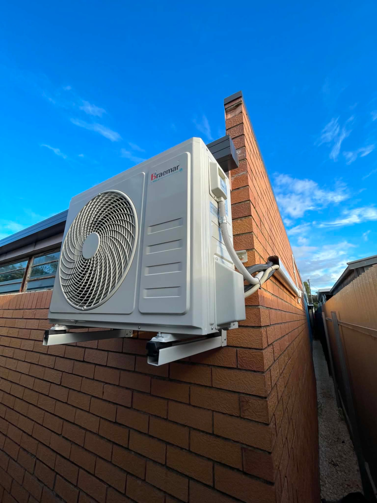 Braemar split system condenser bracket-mounted on a brick wall